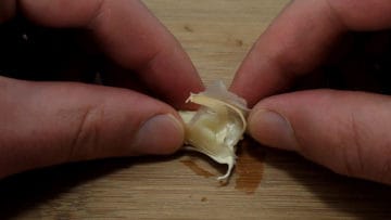 Garlic being peeled with hands. | secretsofcooking.com